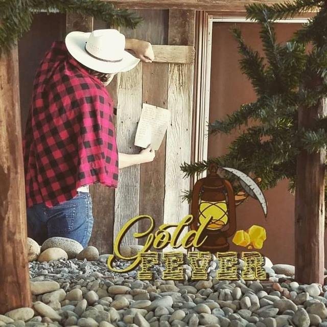 Gold Fever escape room: a prospector in a red plaid shirt and cowboy hat reading a note beside a lantern
